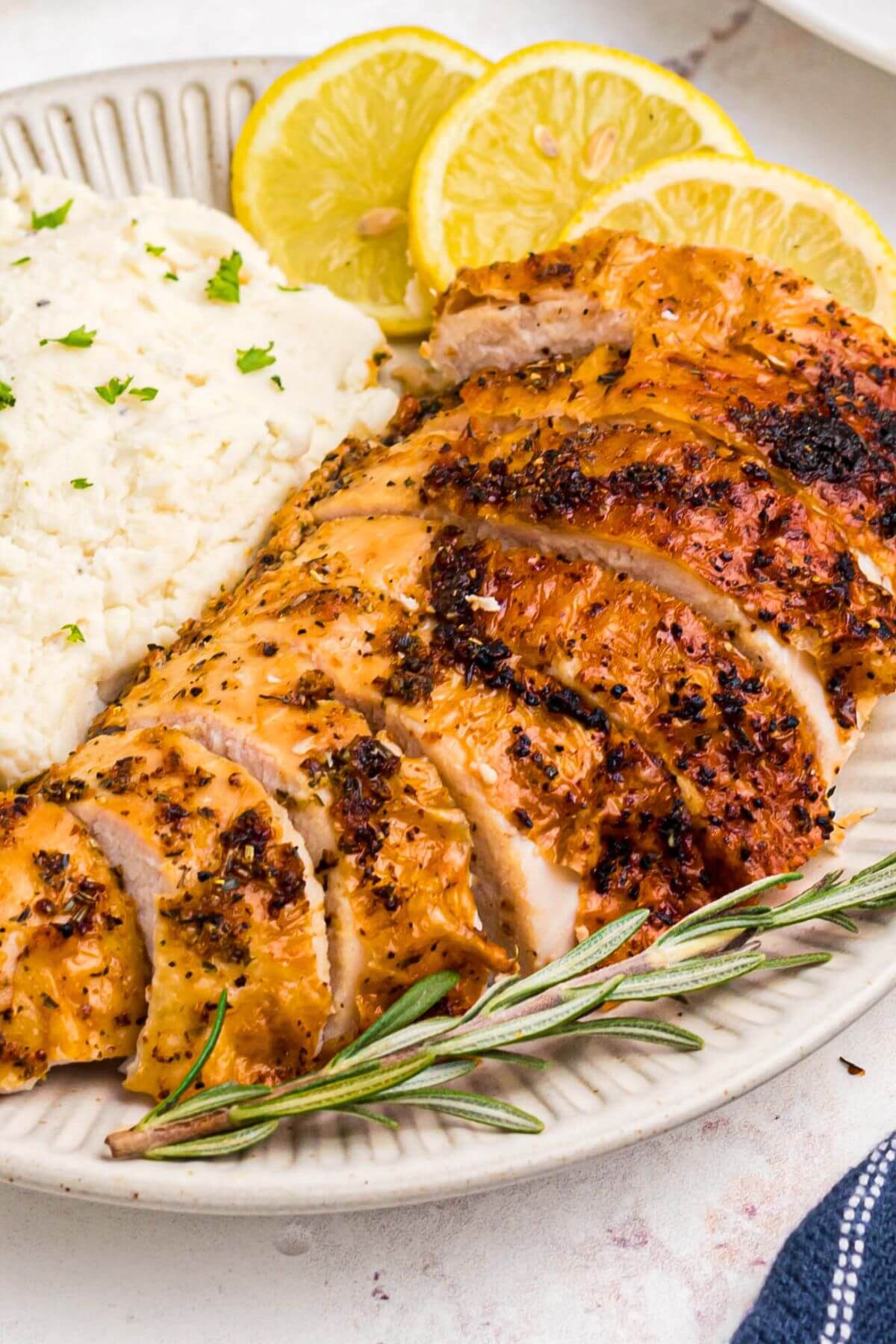 Golden brown turkey breast slices on a white plate with mashed potatoes and lemon slices. 