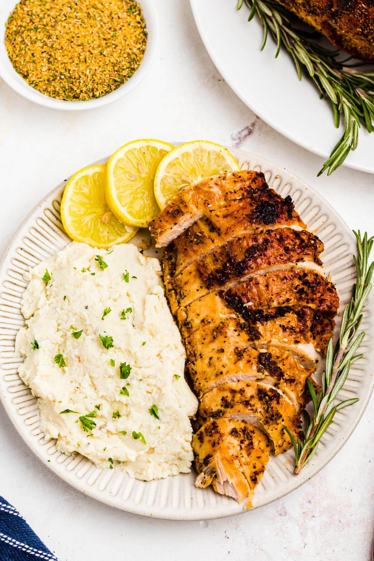 Juicy slices of turkey breast on a white plate with mashed potatoes and lemon slices. 