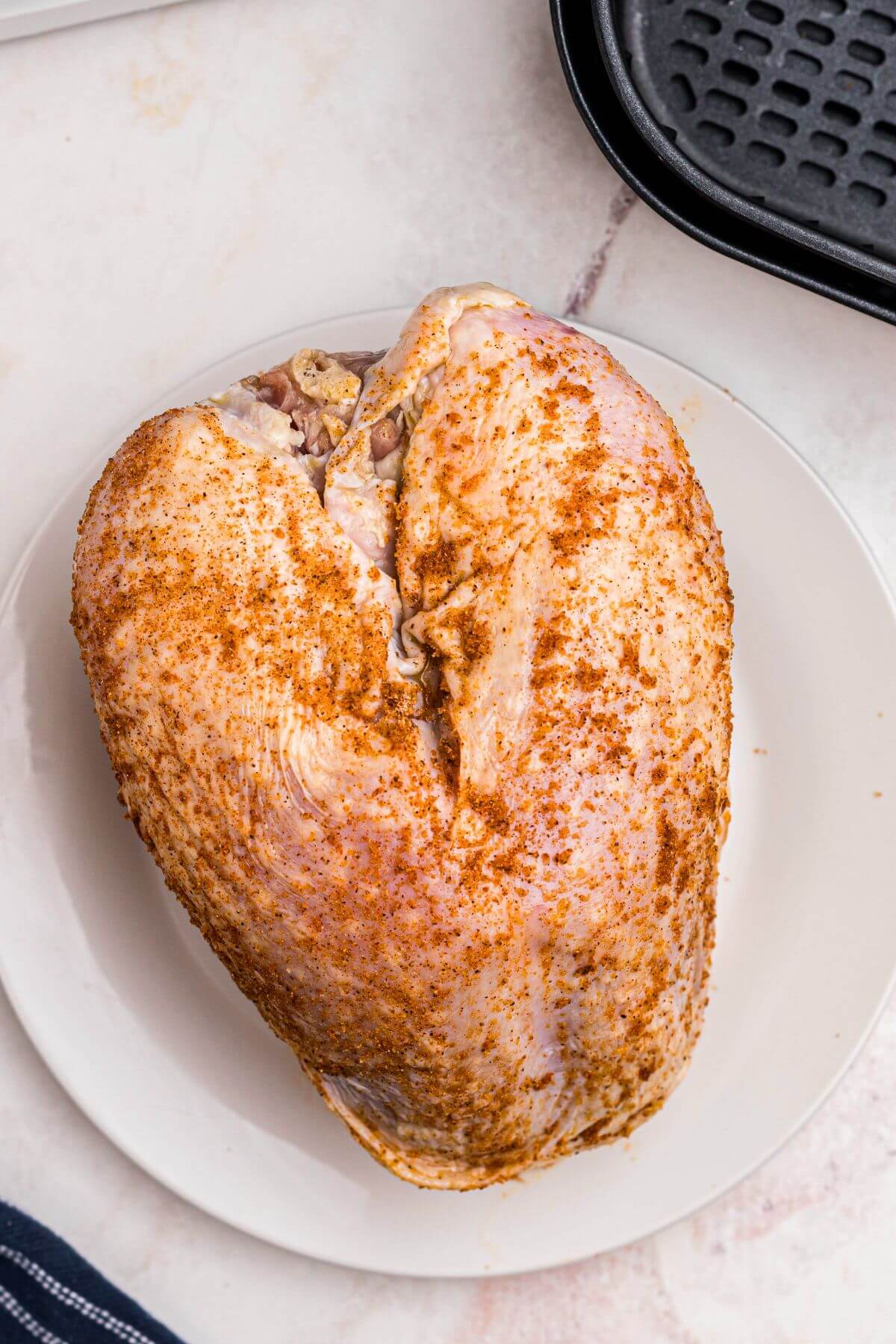 Seasoned uncooked turkey breast in front of the air fryer basket. 