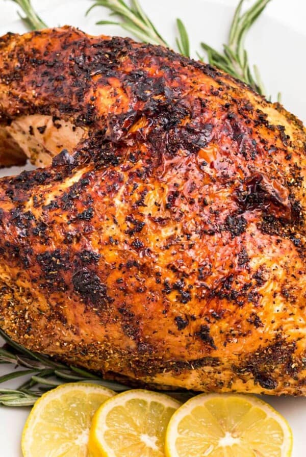 Golden brown seasoned turkey breast on a white plate with lemon slices for garnish.