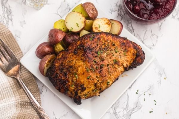 Golden and crispy cooked turkey breast on a white plate served with baby red potatoes and cranberry sauce. 