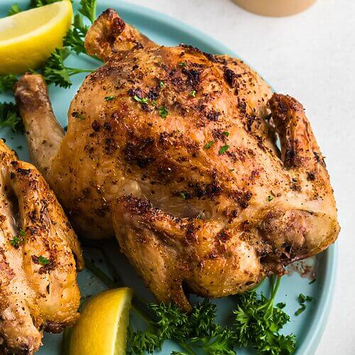 Golden brown crispy Cornish hens on a light blue plate with lemon wedges and parsley garnish.