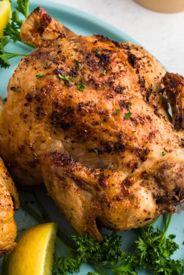 Golden brown crispy Cornish hens on a light blue plate with lemon wedges and parsley garnish.