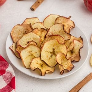 golden apple slices, cooked into chips. Served on a white plate with a red napkin and cinnamon sticks on the table.