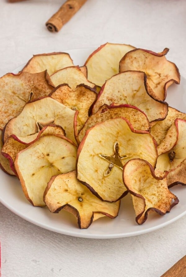 golden apple slices, cooked into chips. Served on a white plate with a red napkin and cinnamon sticks on the table.