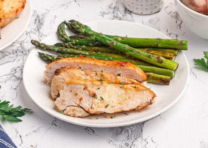 Sliced chicken breast served on a white plate with green asparagus. 