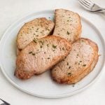 Cooked glazed pork chops cooked and served on a white plate, sprinkled with parsley flakes.