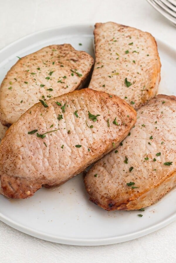 Cooked glazed pork chops cooked and served on a white plate, sprinkled with parsley flakes.