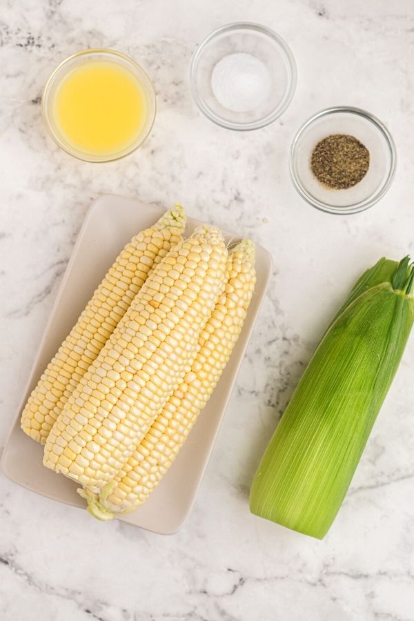 Ingredients needed to make the corn in an air fryer. Melted butter, salt, pepper, and ears of corn. 