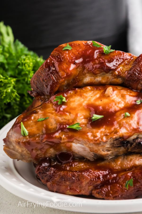Close up of juicy country style ribs basted with bbq sauce and garnished with fresh parsley, served on a white plate. 