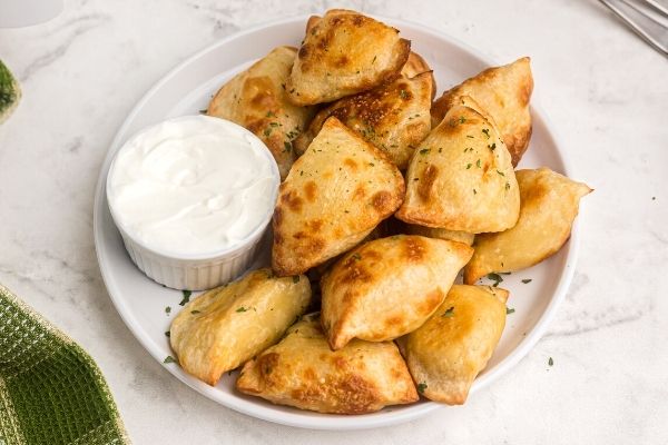 Golden puffed pierogies served on a white plate with a side of sour cream.