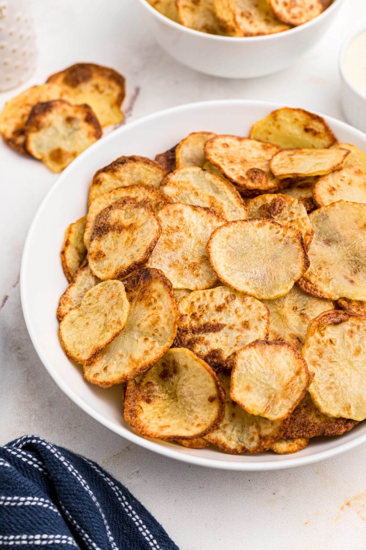 Golden yellow crispy potato chips stacked in a white bowl. 
