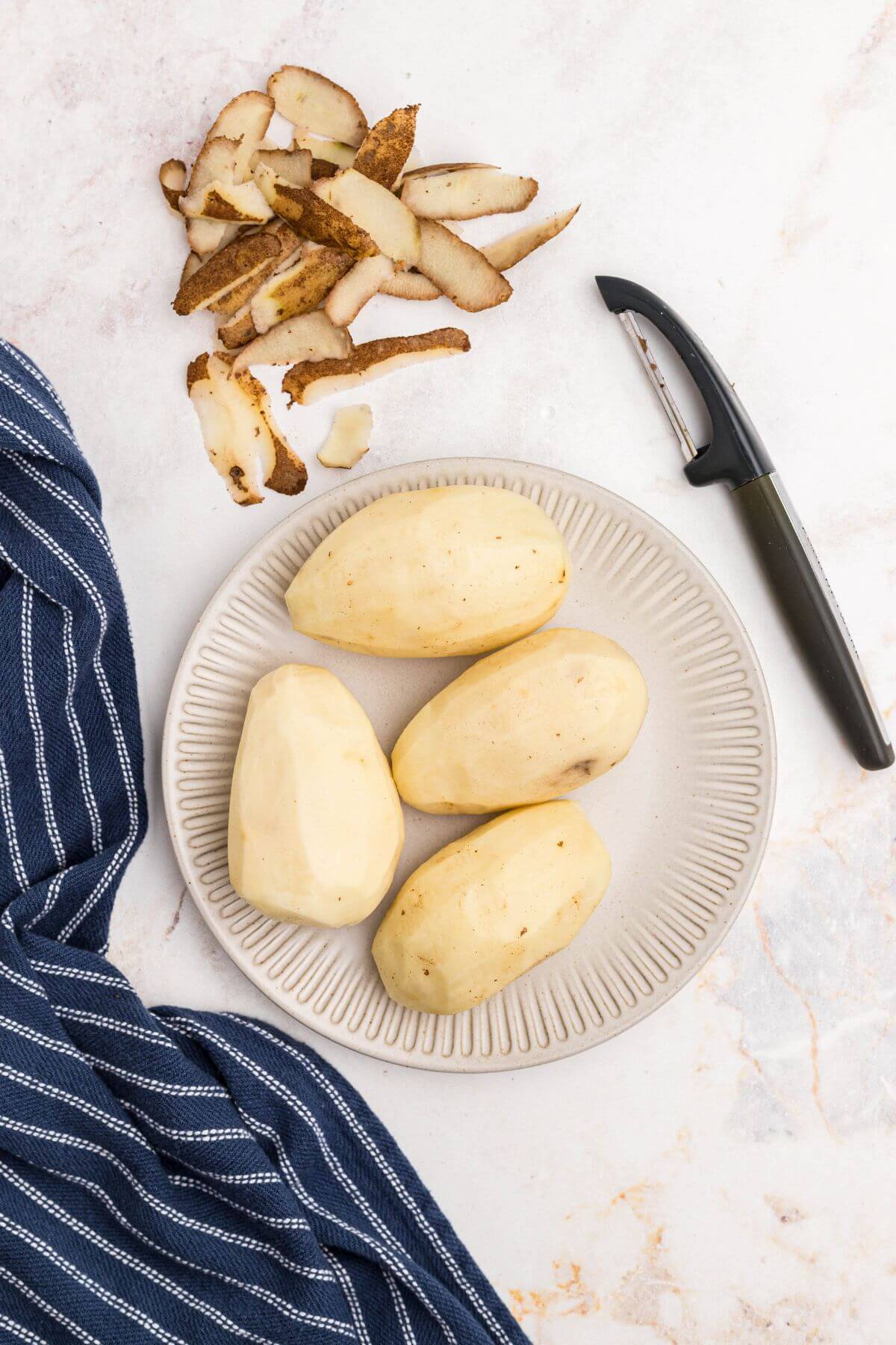 Uncooked potatos, washed and peeled on a marble table. 