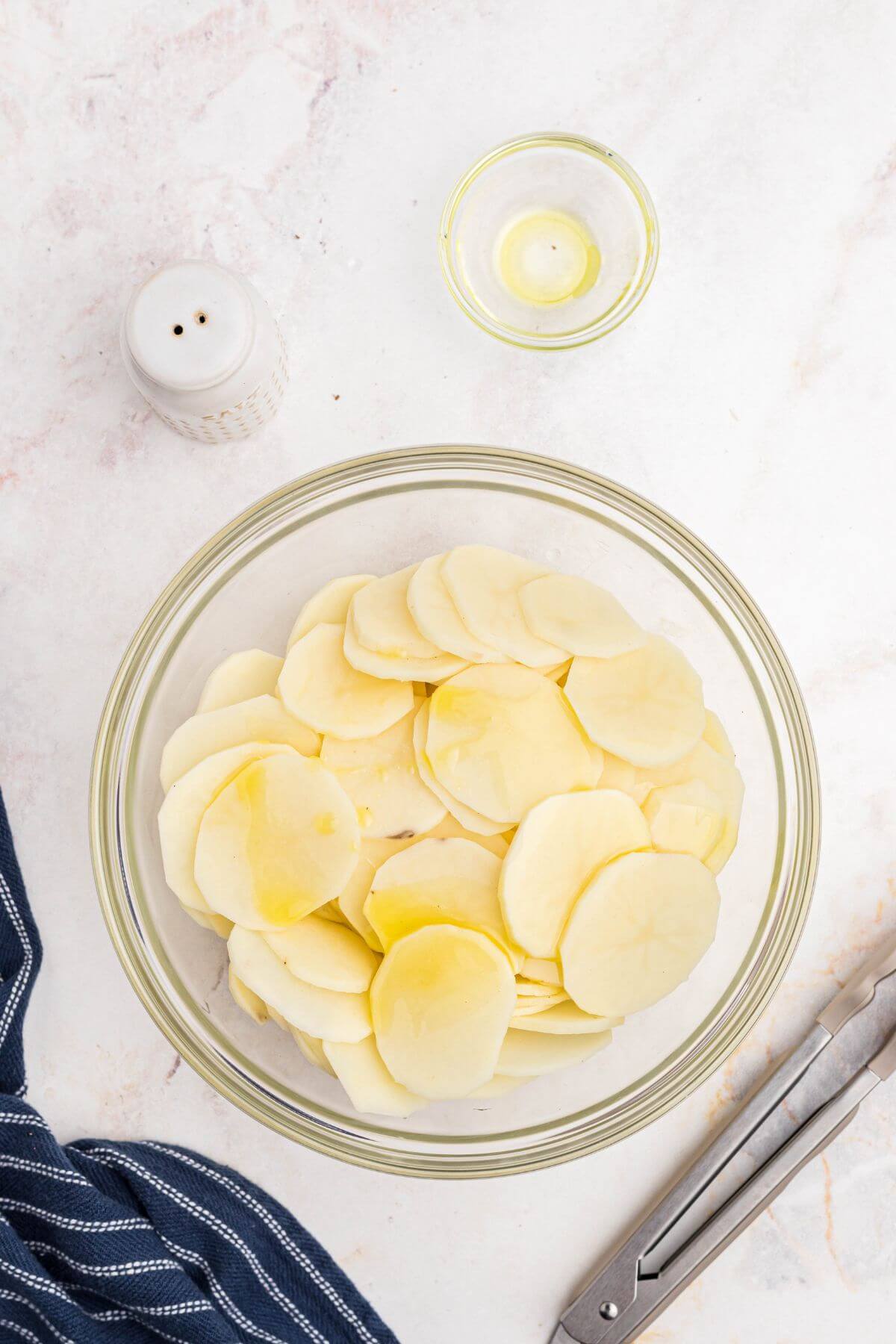 Potato slices in a clear glass bowl with olive oil.