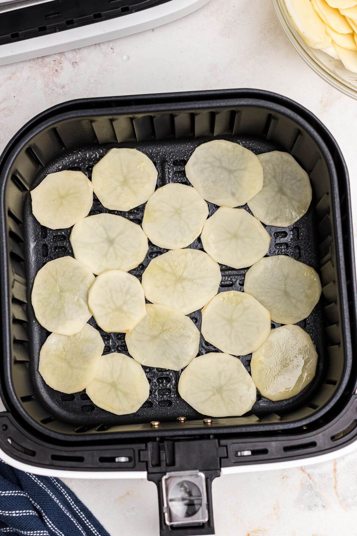 Oiled and seasoned potato slices in the air fryer basket. 