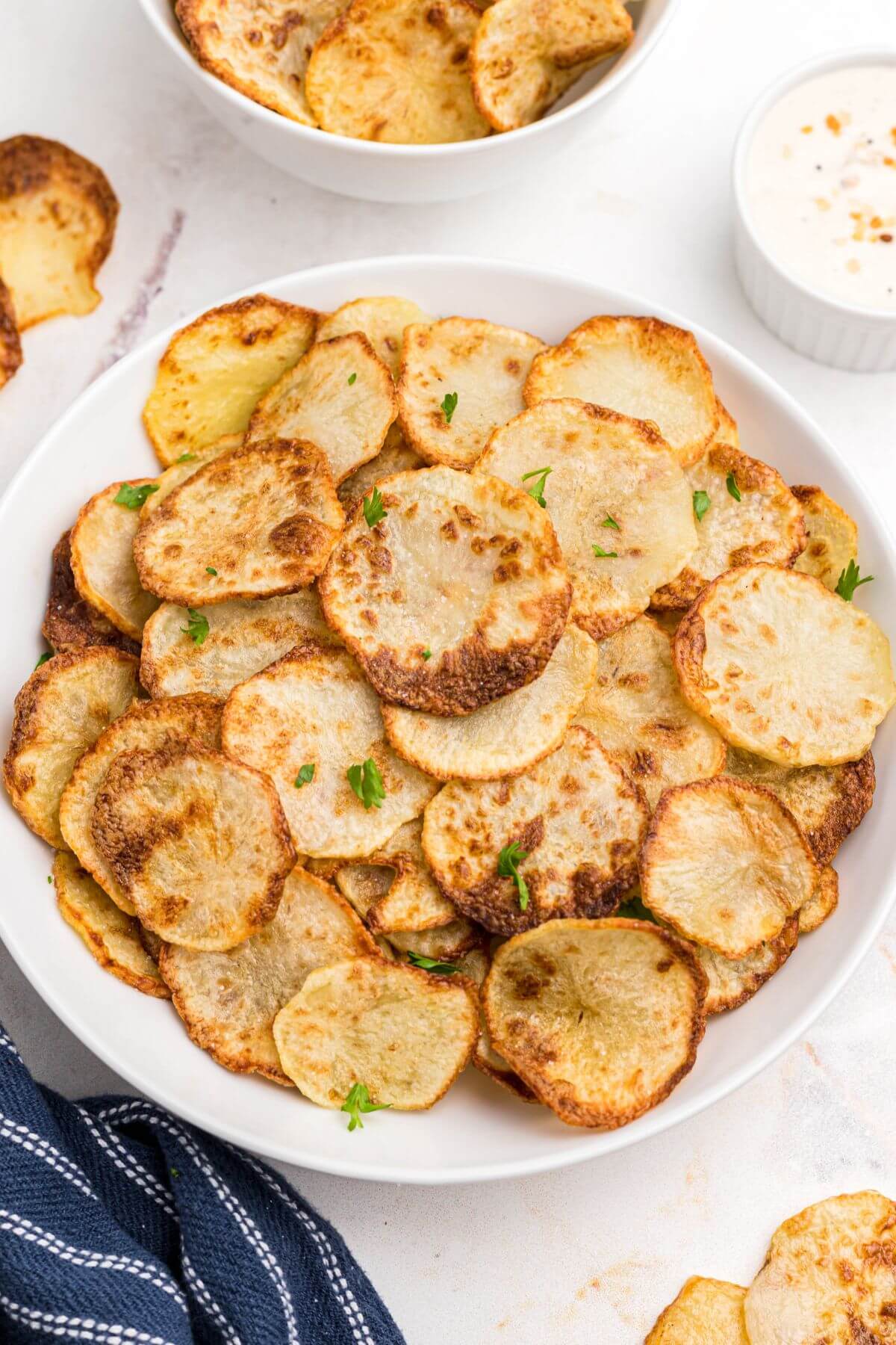 Golden yellow crispy potato chips stacked in a white bowl.