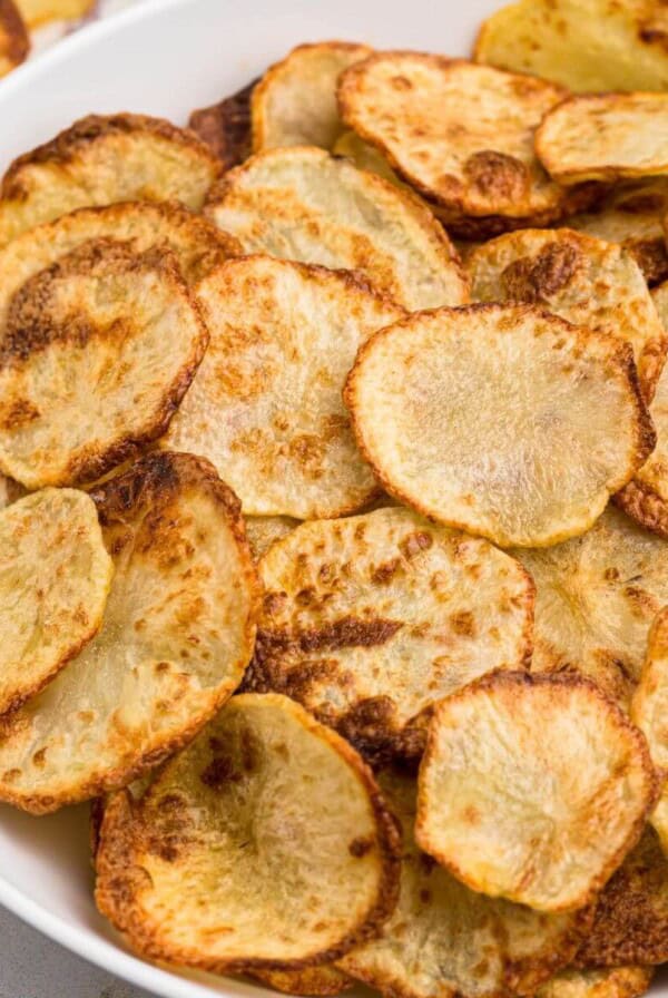 Golden crispy potato chips in a white bowl