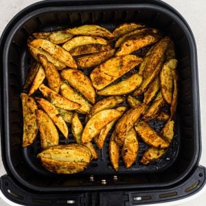 Golden cooked potato wedges seasoned in the air fryer basket.