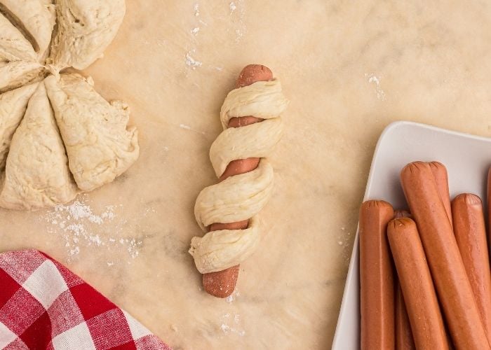 Close up photo of hot dog wrapped in pretzel dough, before cooking. 