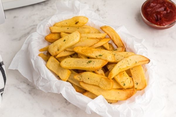 Golden thick cut fries cooked and served in a basket with a side of ketchup. 