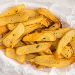 Close up photo of golden crispy steak fries cooked and in a basket, garnished with parsley flakes.