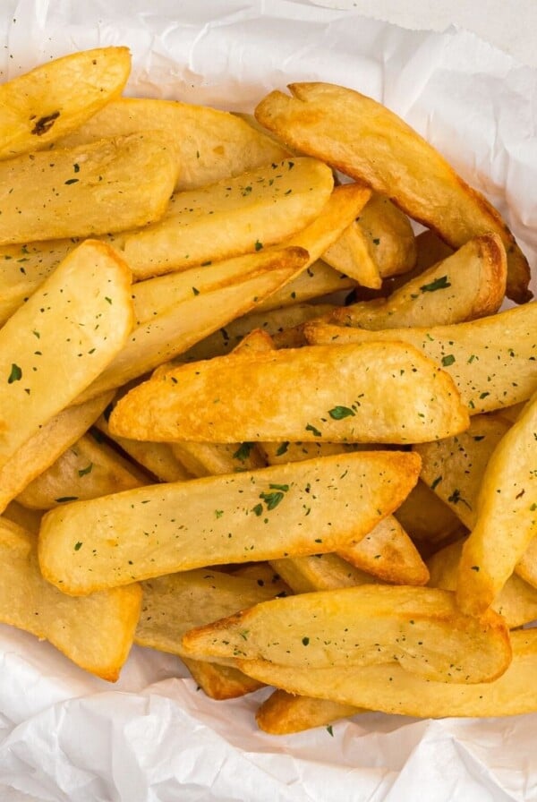 Close up photo of golden crispy steak fries cooked and in a basket, garnished with parsley flakes.