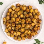 golden cubes of potatoes cut and cooked served on a white plate and garnished with parsley.