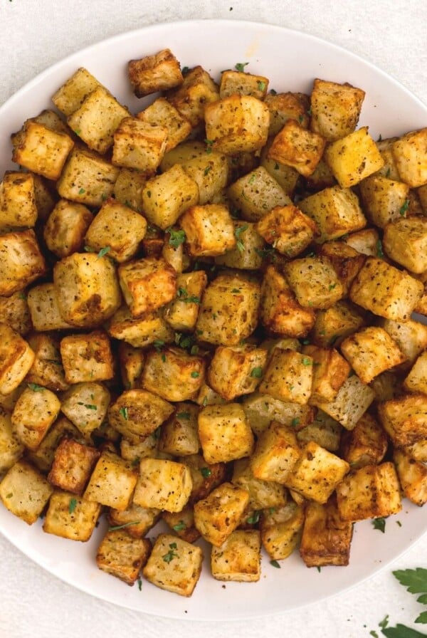 golden cubes of potatoes cut and cooked served on a white plate and garnished with parsley.