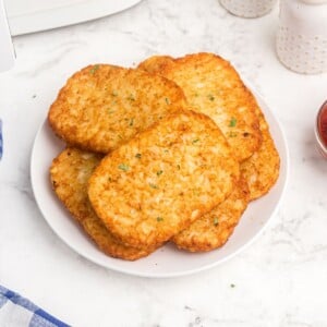 golden hash brown patties on a white plate, served with a side of ketchup.