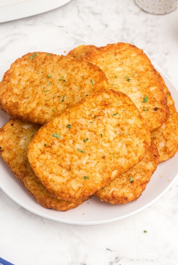 golden hash brown patties on a white plate, served with a side of ketchup.