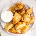 Golden and puffy, cooked pierogies served on a white plate with a side of sour cream.