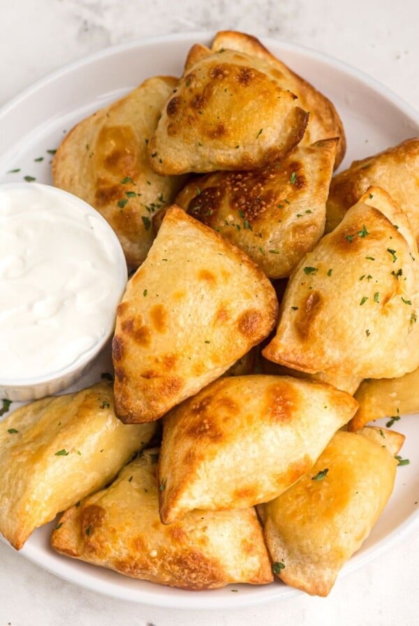 Golden and puffy, cooked pierogies served on a white plate with a side of sour cream.