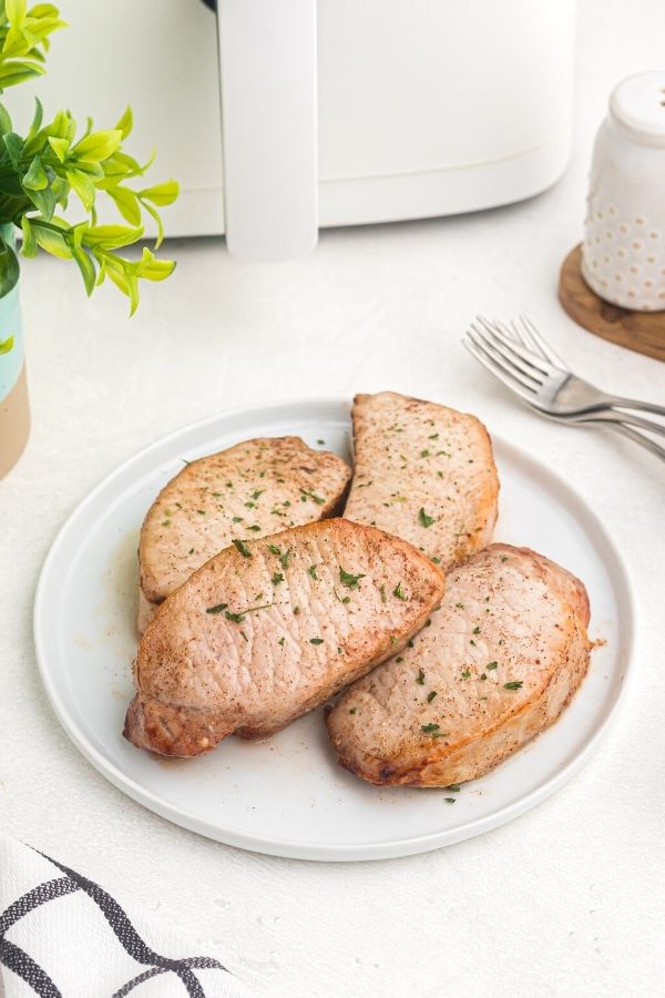 Glazed pork chops on a white plate garnished with parsley flakes