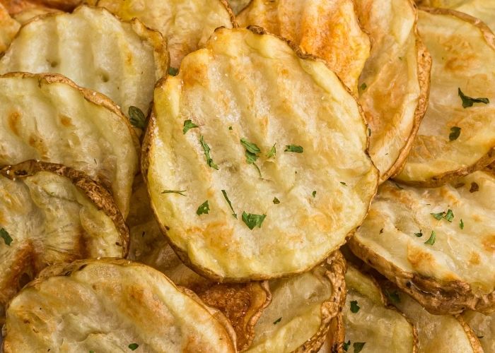 Close up photo of golden potato chips sprinkled with parsley flakes. 