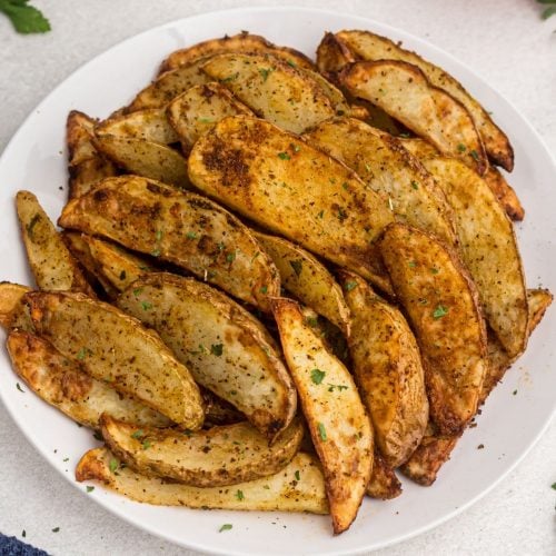 golden cooked potato wedges on a white plate showing parsley flakes as a garnish.