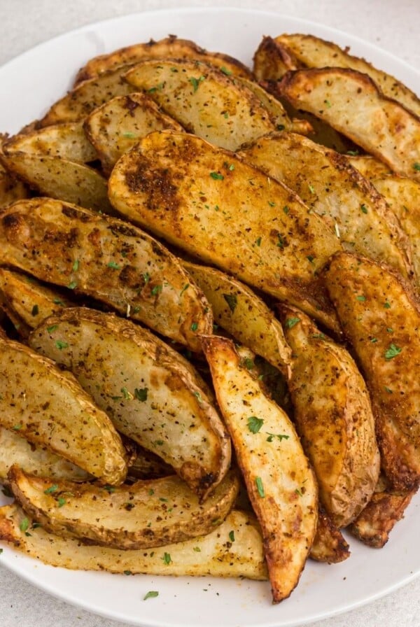 golden cooked potato wedges on a white plate showing parsley flakes as a garnish.