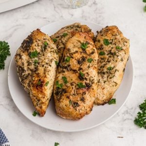 golden chicken breasts seasoned and served on a white plate with parsley garnish.