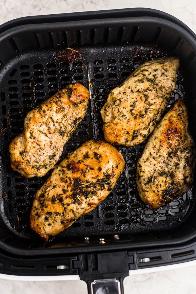 Golden juicy and seasoned chicken breasts in an air fryer basket after being cooked.