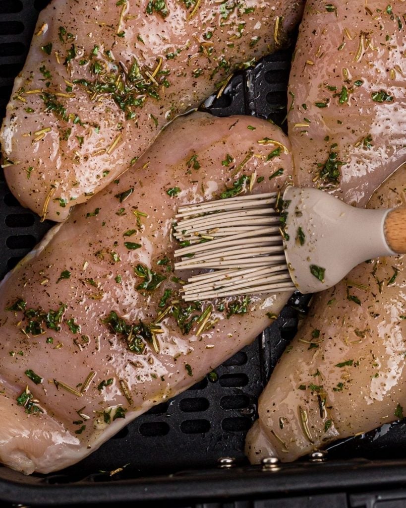 Pastry brush being used to brush each piece of chicken before being cooked in the air fryer basket. 