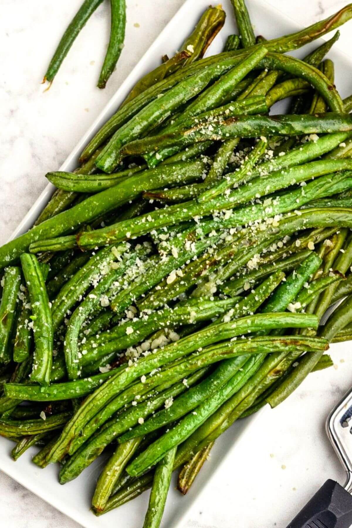 Green juicy green beans stacked on a white rectangle plate seasoned and sprinkled with grated parmesan cheese. 