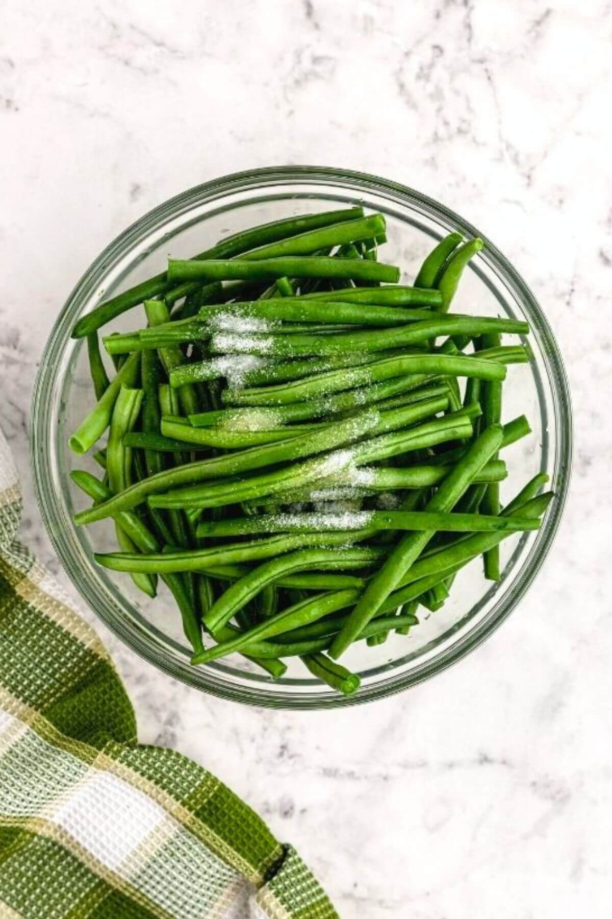 Trimmed green beans in a clear bowl tossed with olive oil and seasonings. 