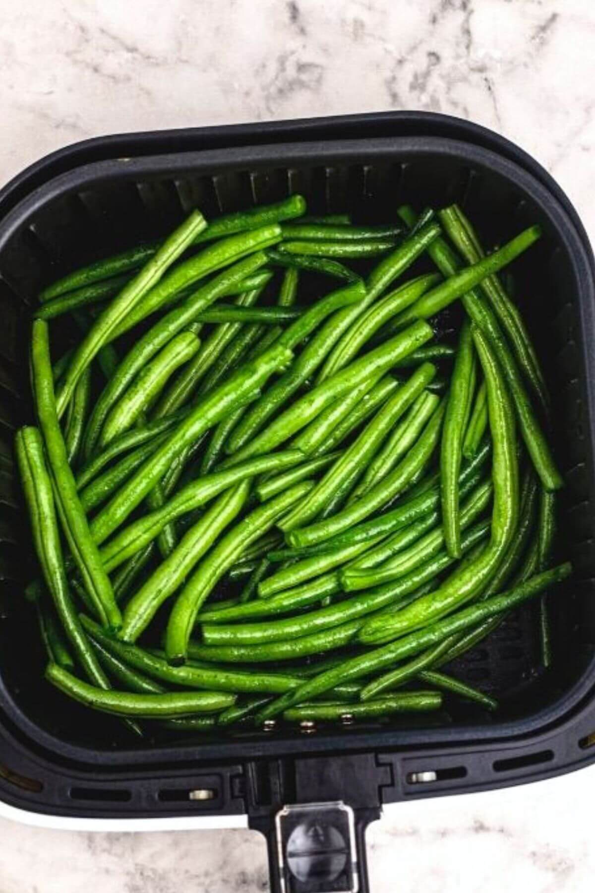 Seasoned green beans in the air fryer basket before being cooked. 