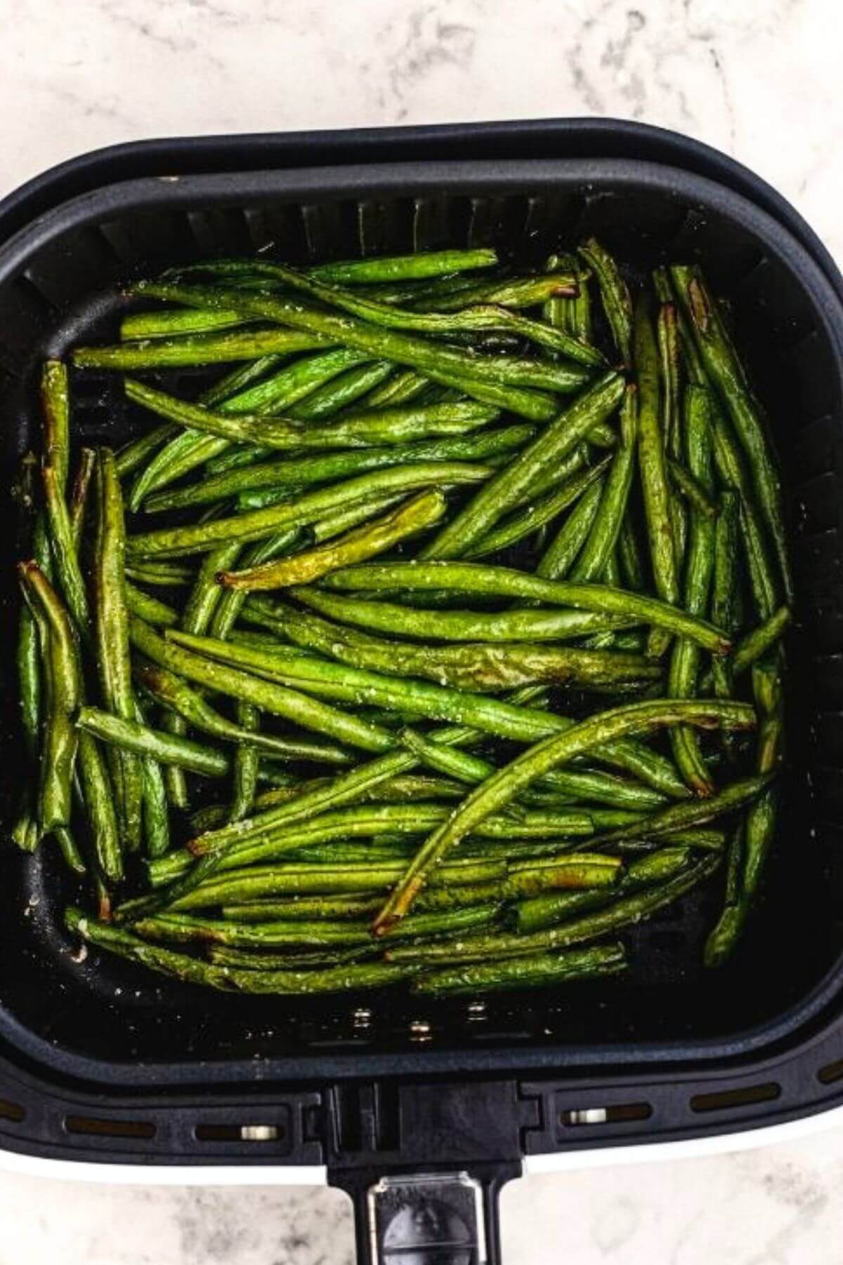 Juicy and crispy cooked green beans in the air fryer basket. 