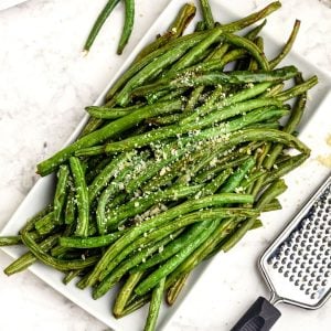 Green beans cooked on a white plate, grated with parmesan cheese.