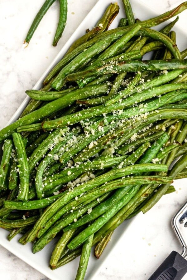 Green beans cooked on a white plate, grated with parmesan cheese.