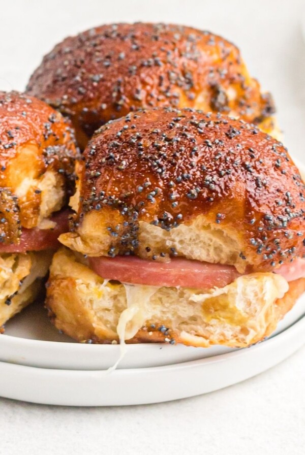 Close up photo of golden small roll with ham and swiss cheese inside, glazed with a poppyseed glaze.