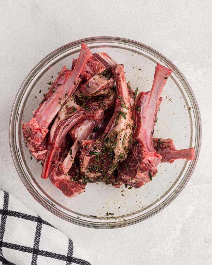 lamb chops in a glass bowl tossed with olive oil and seasonings. 