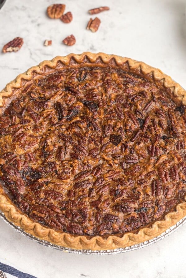 Golden pecan pie on a white marble table with scattered pecans around the pie plate.