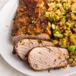 Golden juicy and seasoned pork tenderloin, sliced and served on a white plate with stuffing.