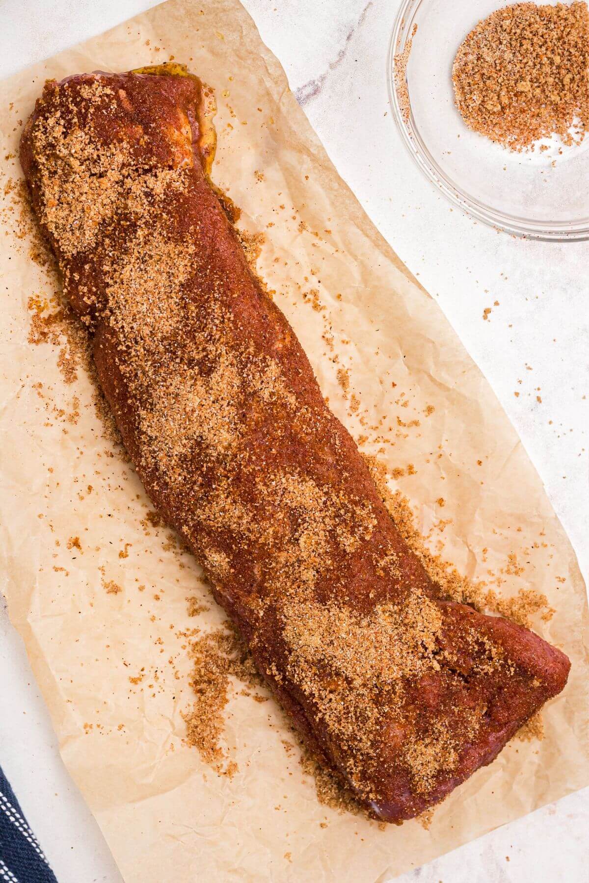Uncooked pork tenderloin on light brown butcher paper, after being seasoned with brown sugar and spices. 